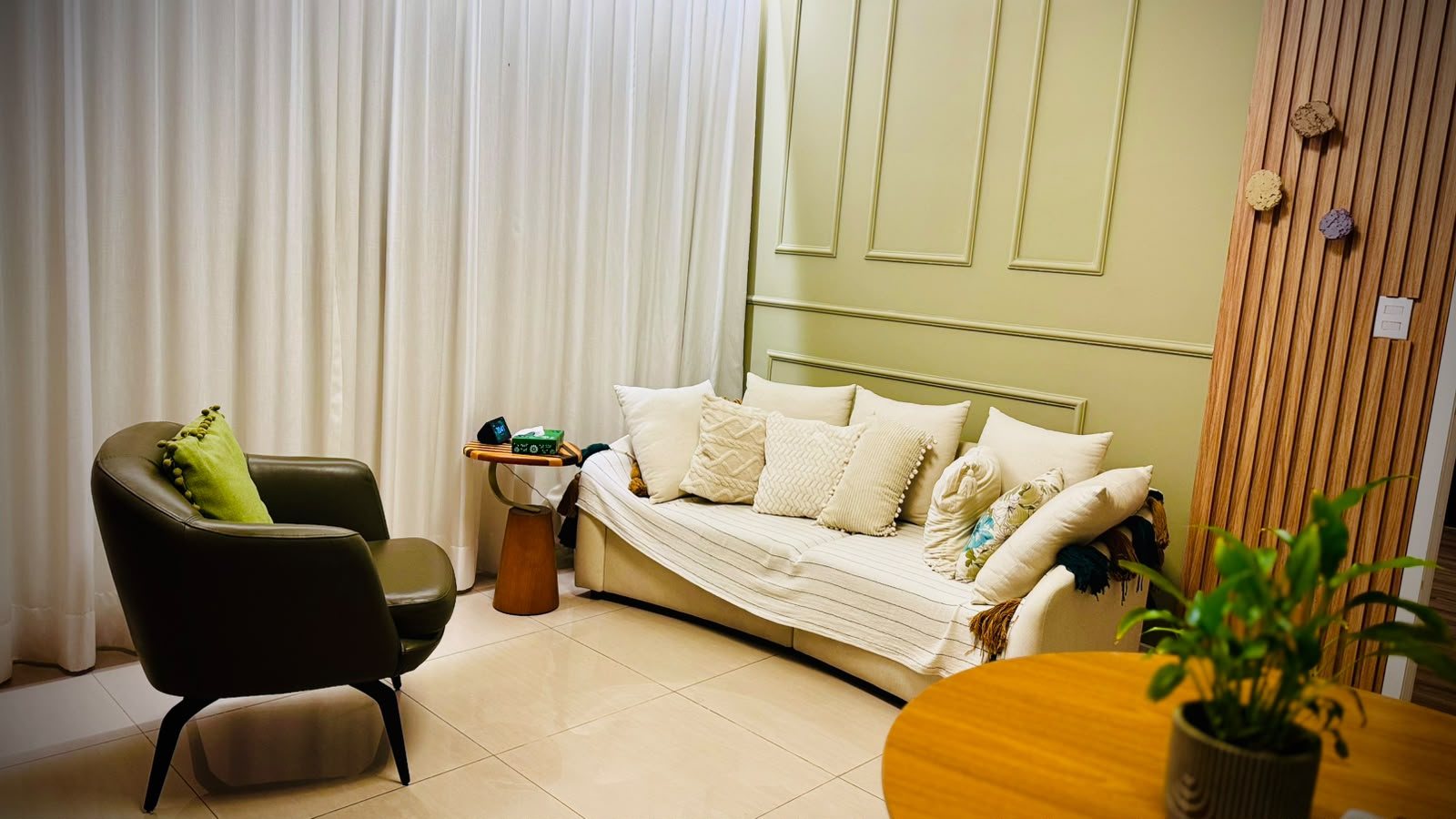 Consultório do Instituto Ser: sofá claro, poltrona de couro e parede verde com boiserie