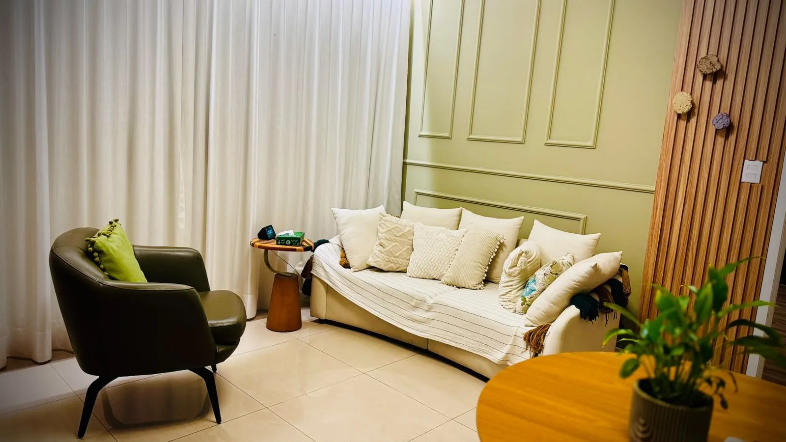 Consultório do Instituto Ser: sofá claro, poltrona de couro e parede verde com boiserie