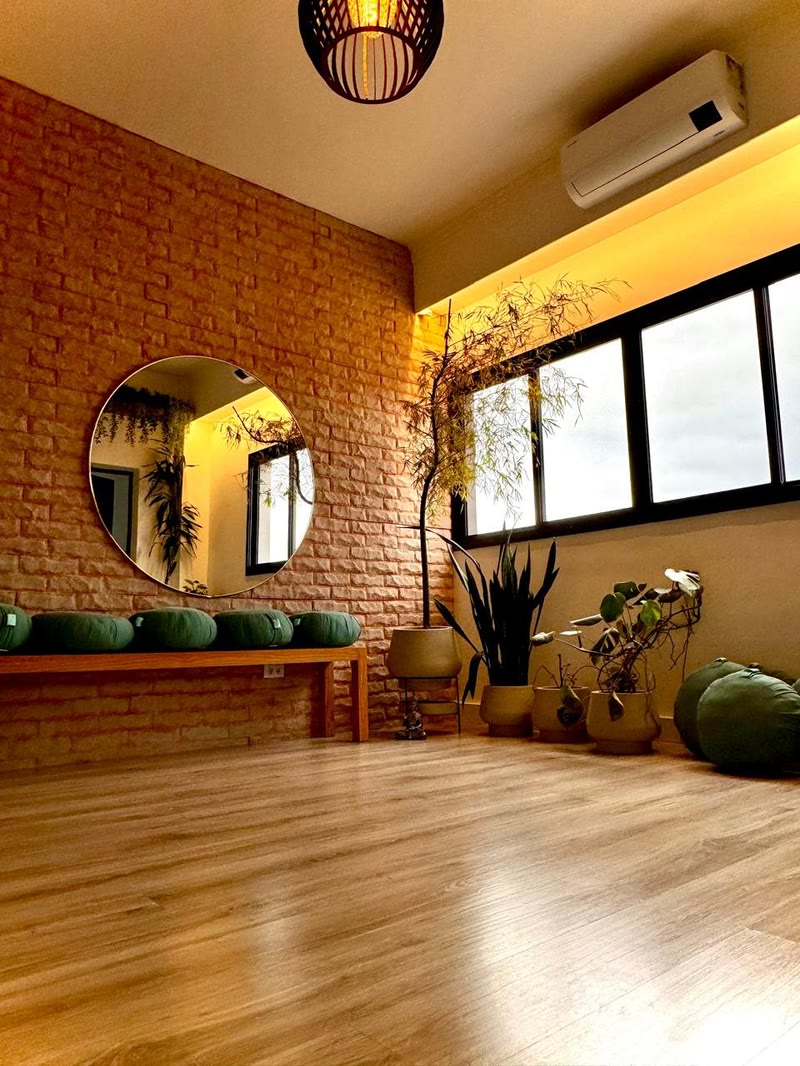 Sala de práticas com espelho redondo, almofadas de meditação e plantas